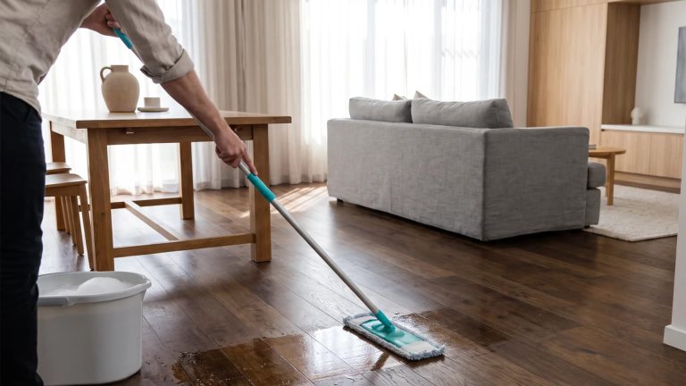Person mopping a clean hardwood floor with a flat microfiber mop in a bright living room.