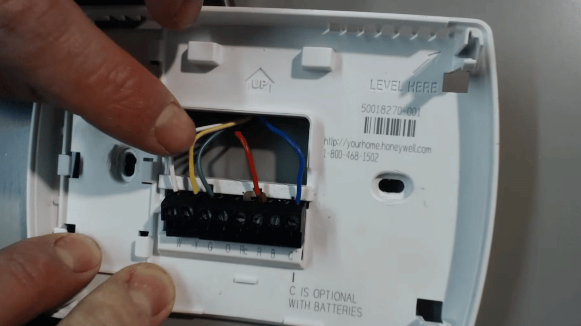 hand pointing to colored thermostat wires connected to labeled HVAC terminals on the wall base