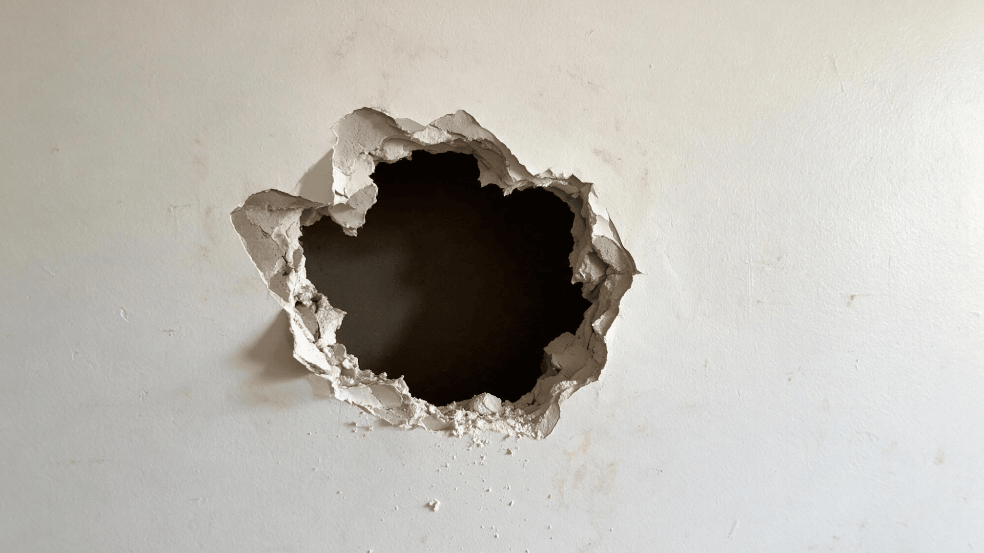 large hole in drywall wall exposing dark cavity behind