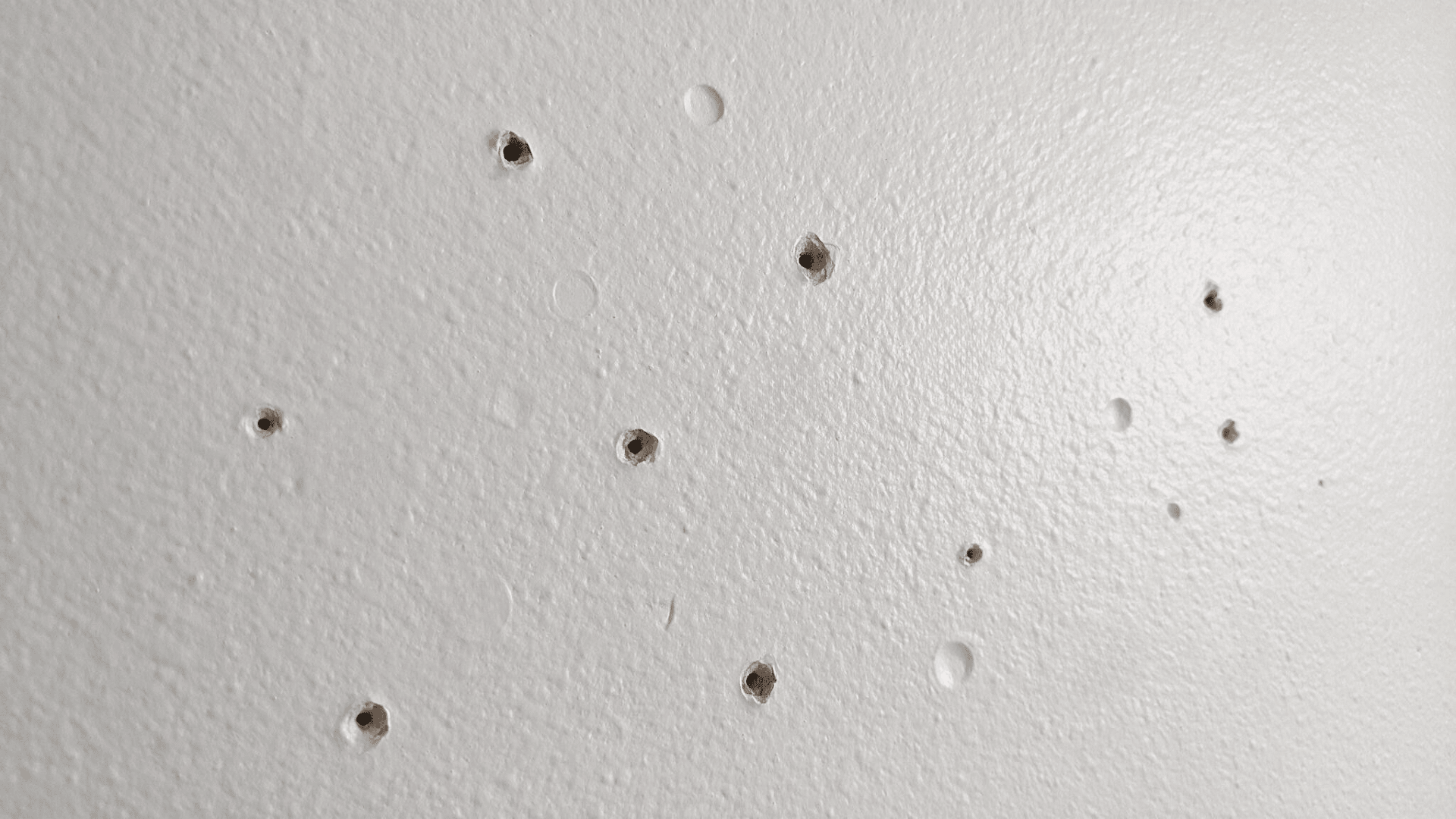 small nail holes and dents on a textured white drywall wall
