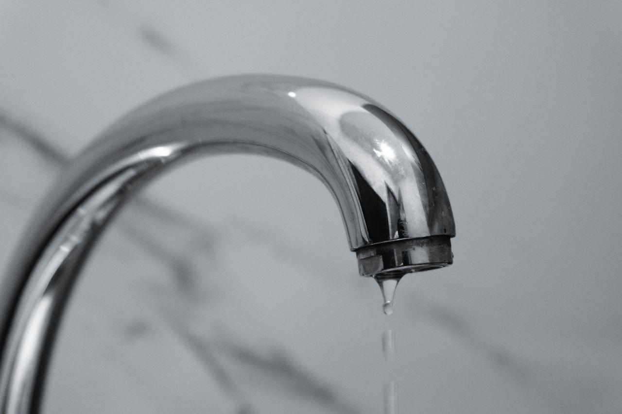 Dripping chrome faucet against light gray background in close-up view