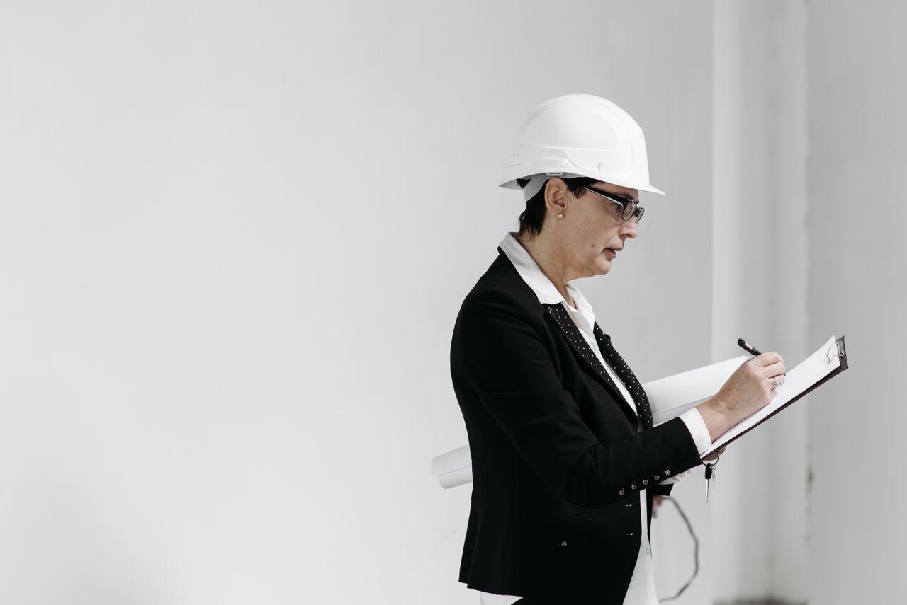 Construction worker in white hard hat writing on clipboard in minimalist interior space