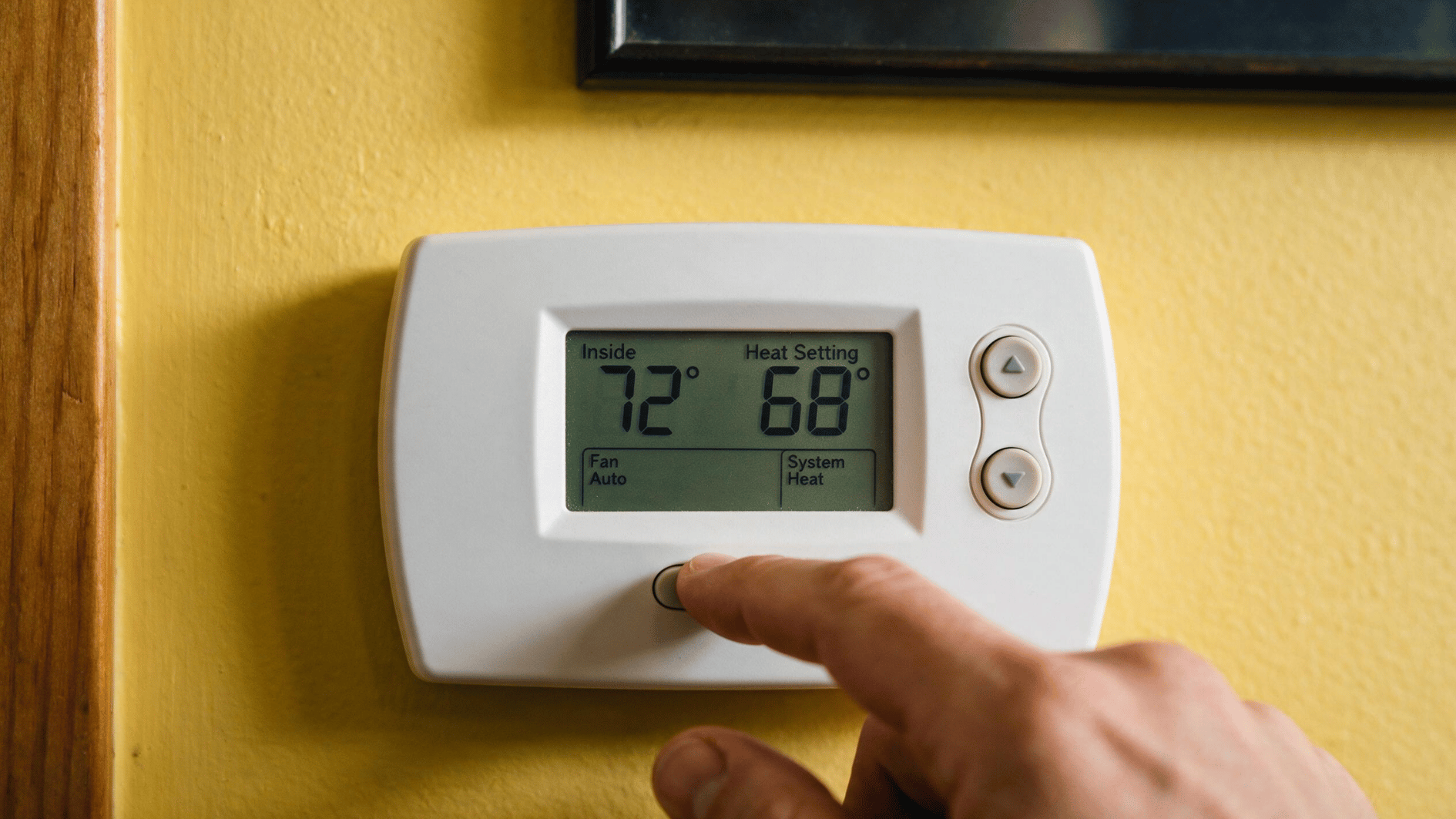 hand adjusting a digital wall thermostat set to heat mode with the indoor temperature shown at 72 degrees