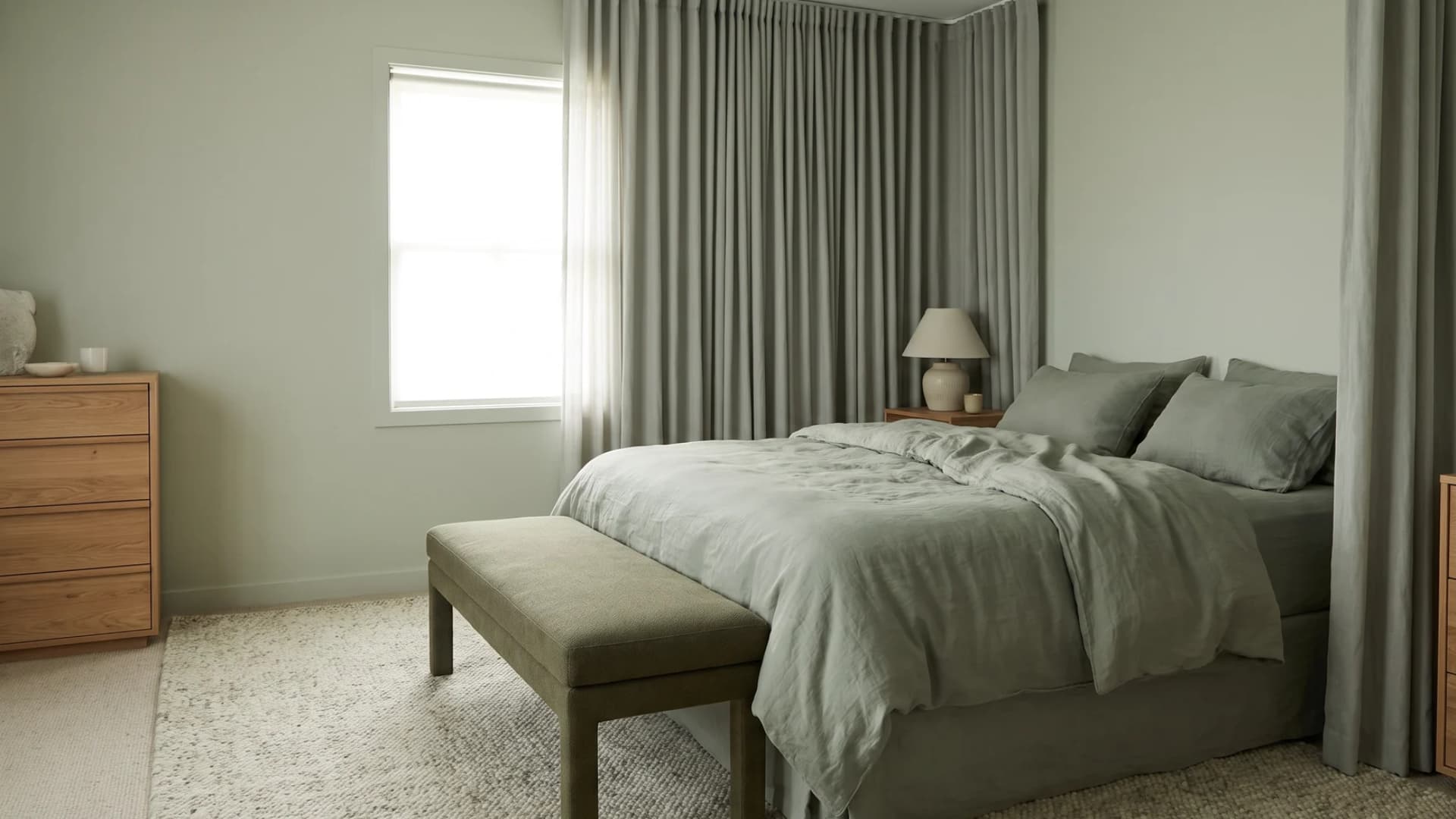 Sage green bedroom featuring layered linen bedding, wooden furniture, and soft green walls.
