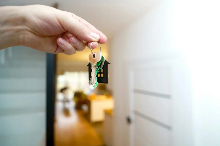 Hand holding house keys with a keychain shaped like a house in bright living room