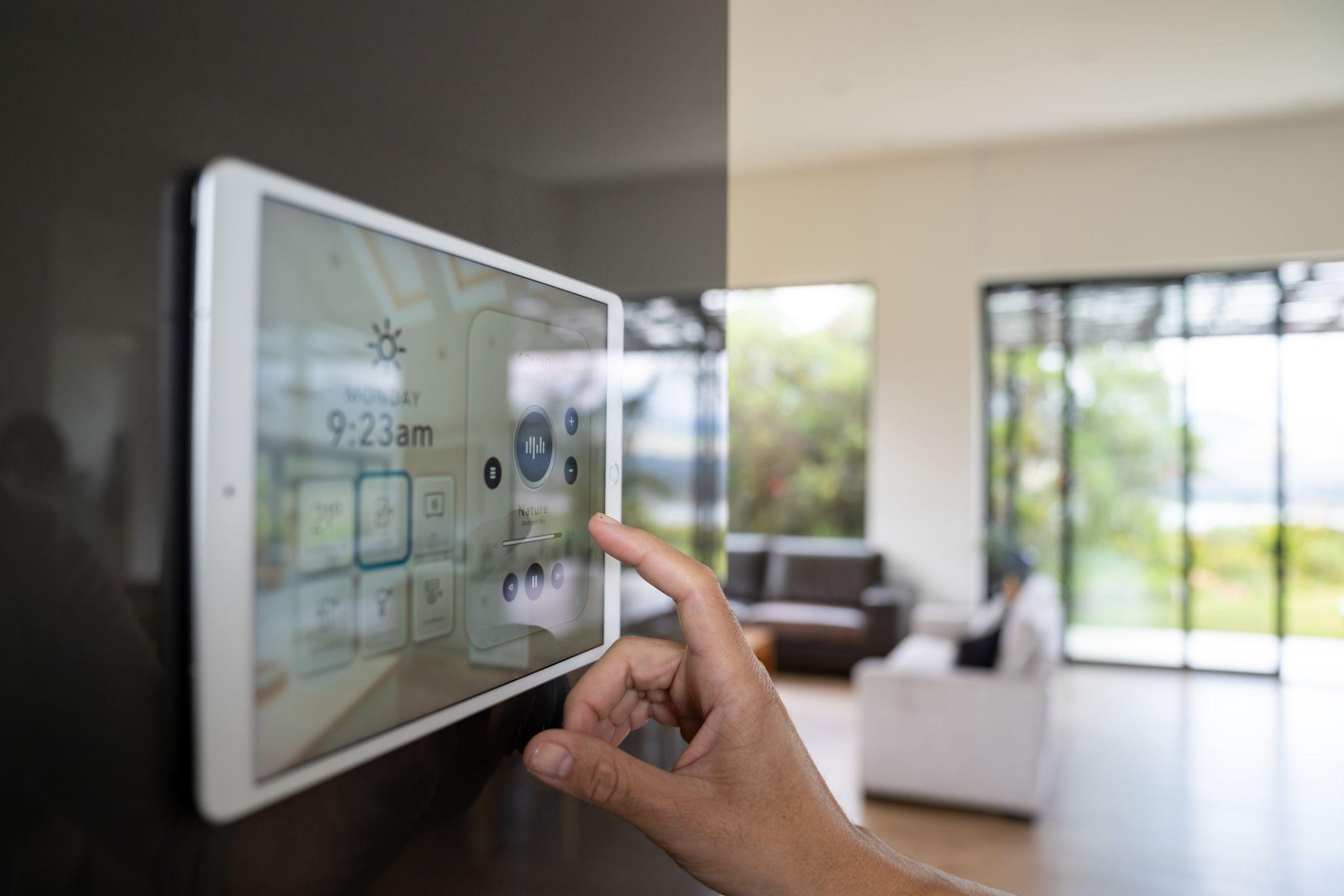 Hand operating smart home control panel in modern living room with large windows