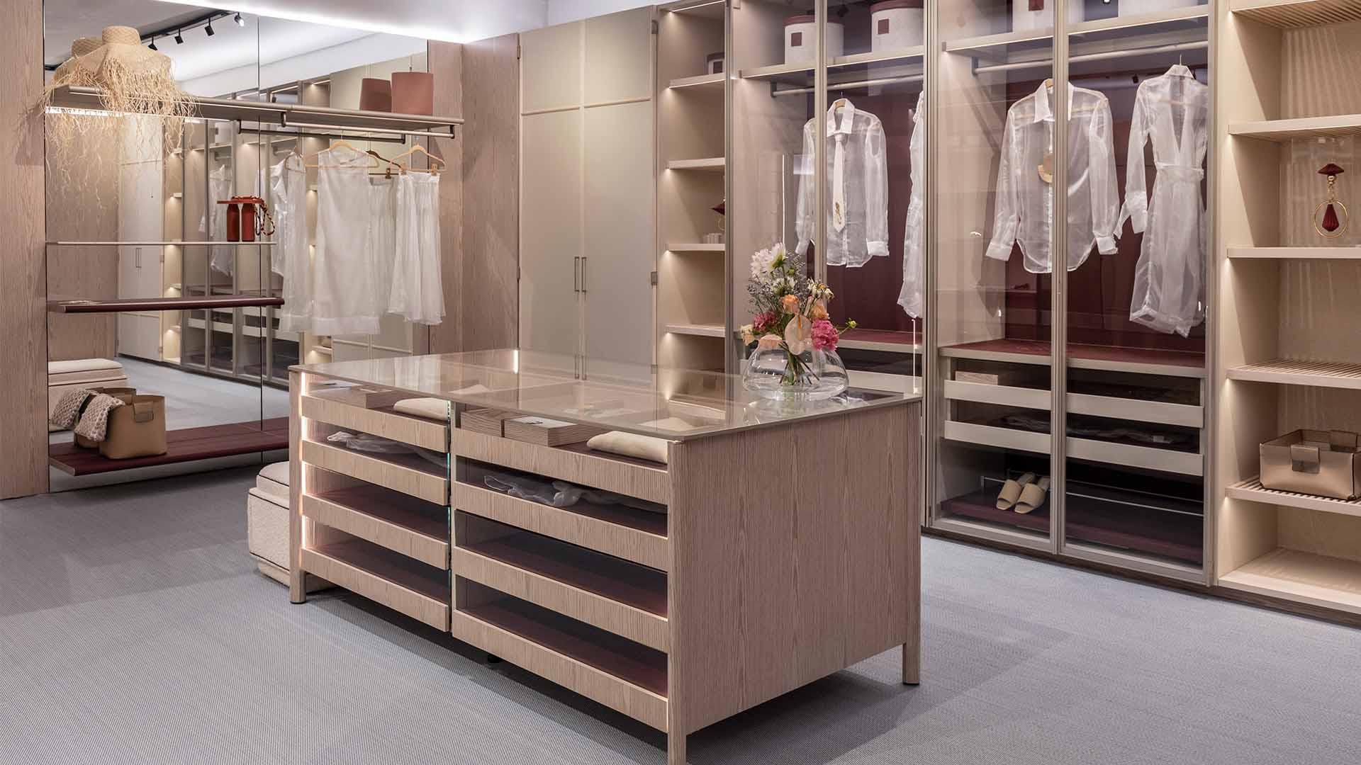 Modern walk-in closet with glass-topped wooden island and hanging sheer garments