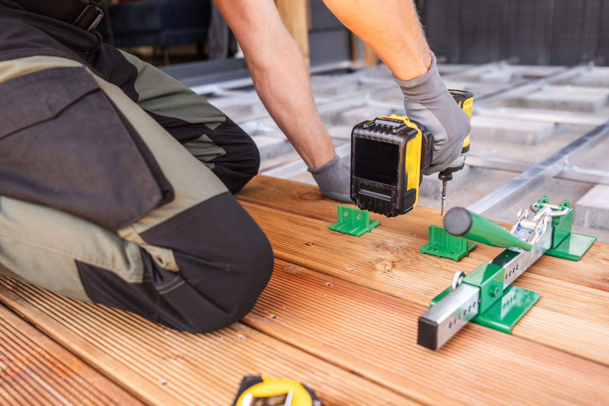 Worker using power drill on wooden deck with green brackets outdoors