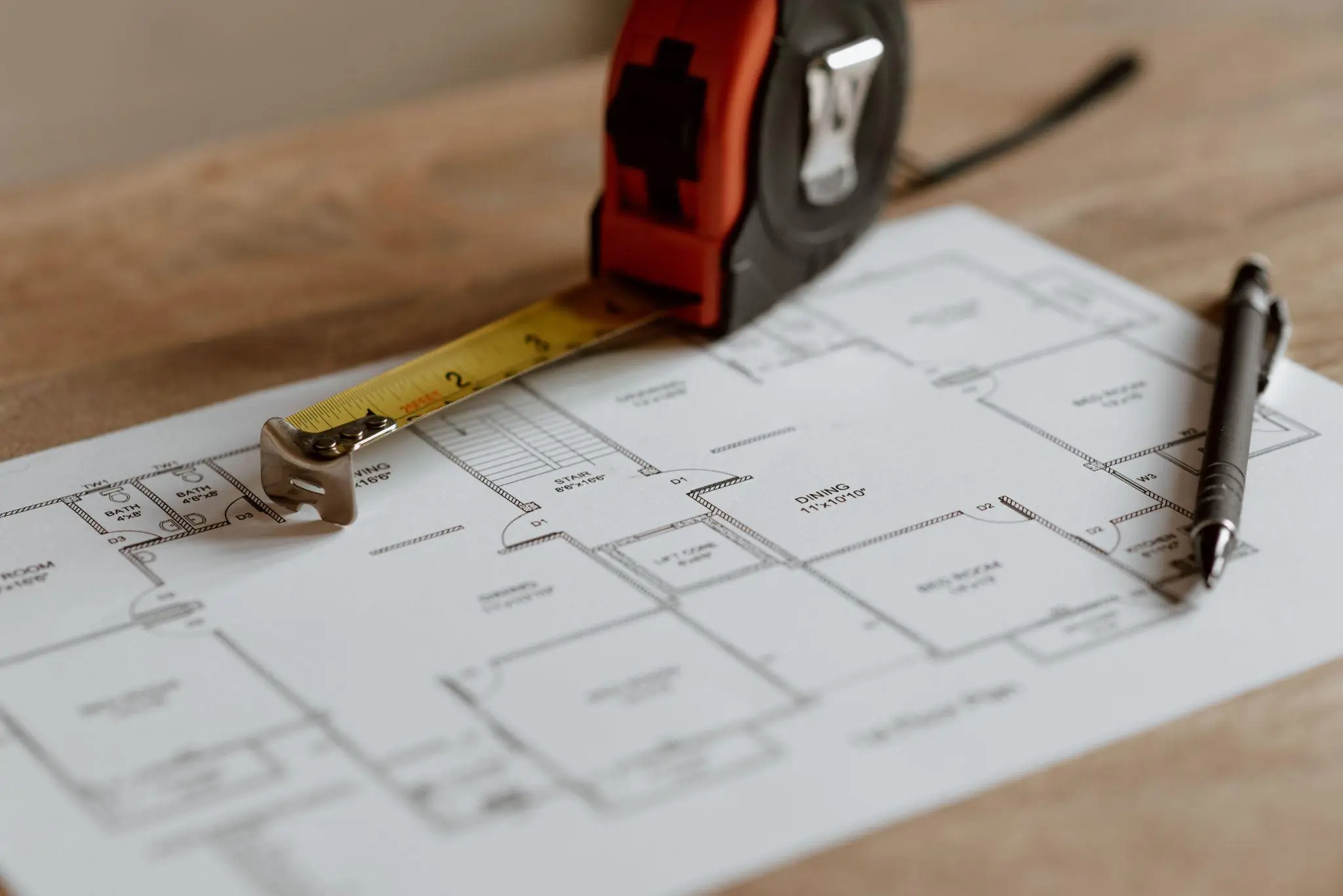 Tape measure and pen on architectural floor plan on wooden surface