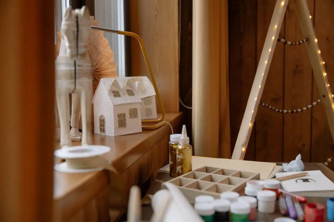 Craft supplies and a small decorative house on wooden table with warm lighting