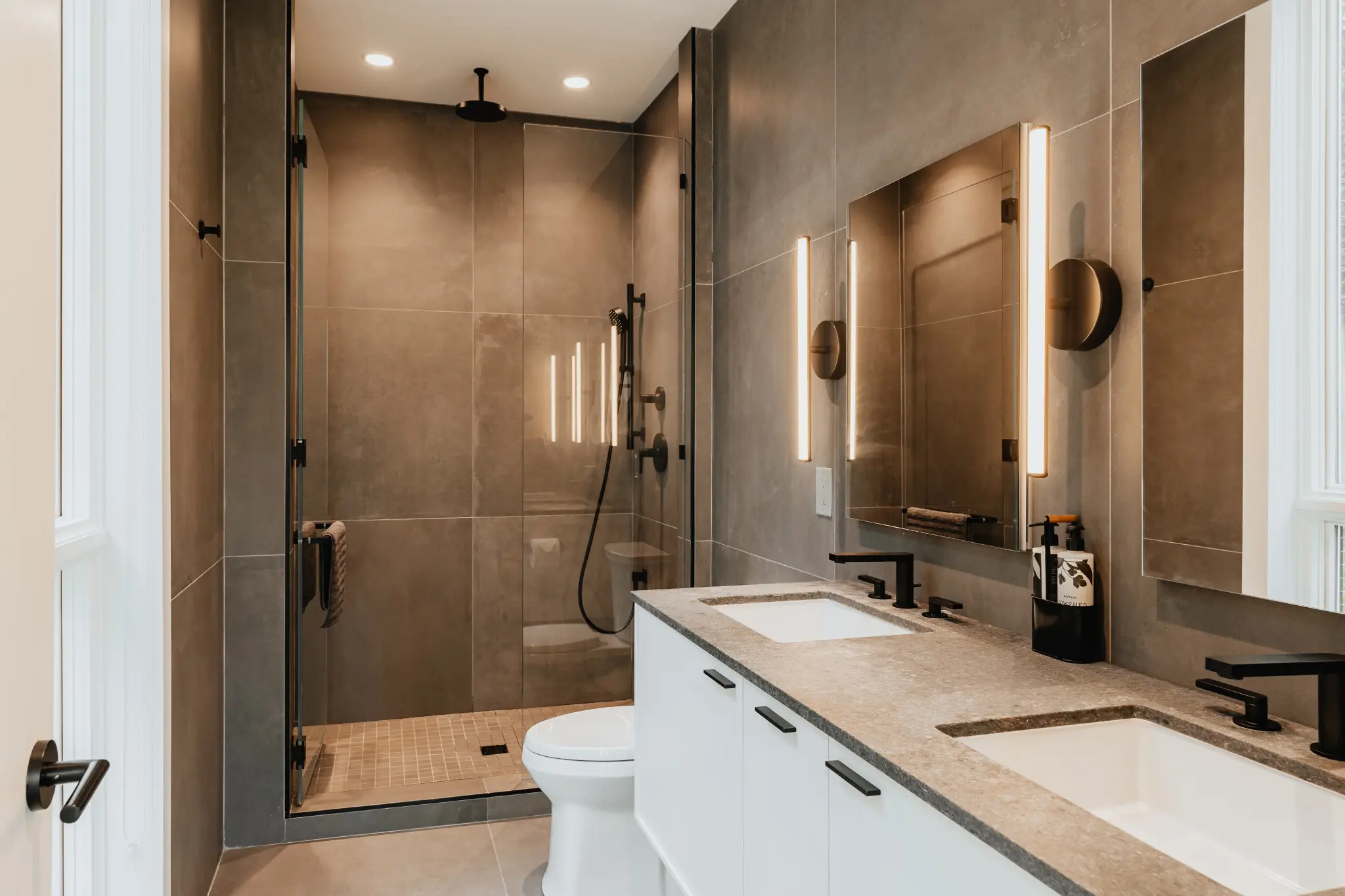 Modern bathroom with double sinks, large mirror, and walk-in shower in neutral tones